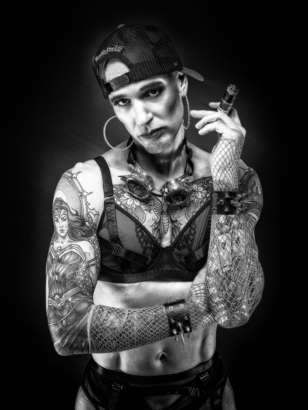 Studio-Nahaufnahme eines tätowierten Models mit Cigarre im Netzoutfit – queeres Fetischporträt von Hell On Heels Photography Düsseldorf