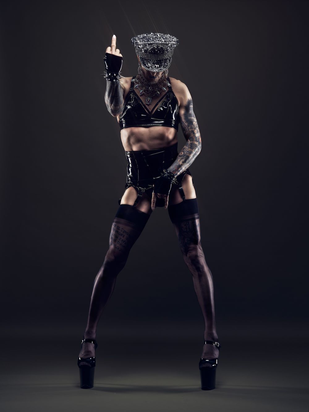 Ganzkörper-Fetischporträt mit Glitzerhut, Lackmode und Mittelfinger-Geste – Fotograf Tobias Prümm in Düsseldorf