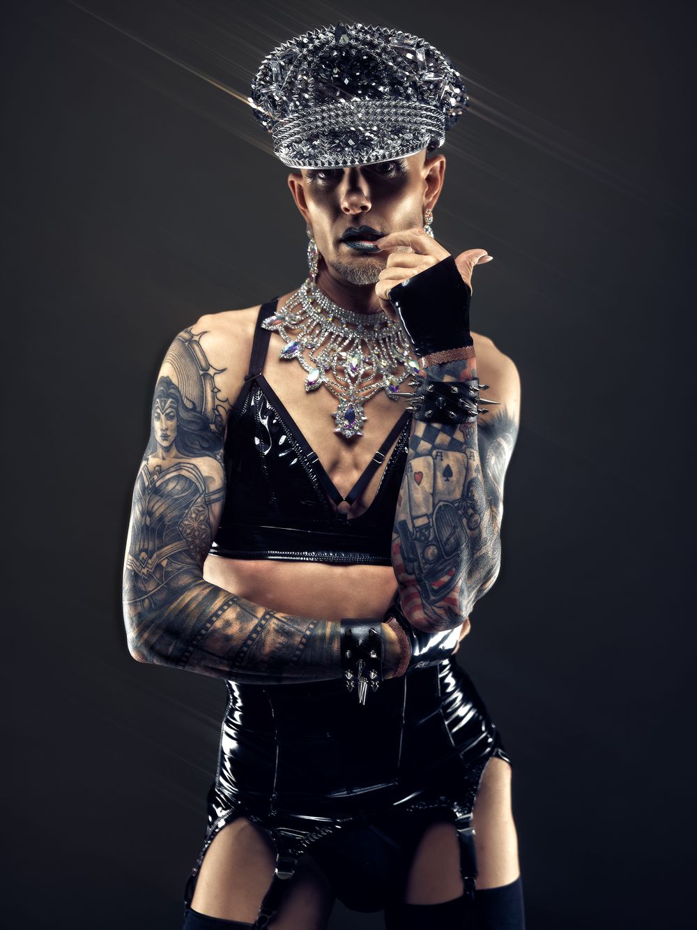 Queeres Studio-Porträt eines tätowierten Models mit Lack-Outfit und Glitzerhut – Fetischfotografie von Hell On Heels Photography Düsseldorf und Köln
