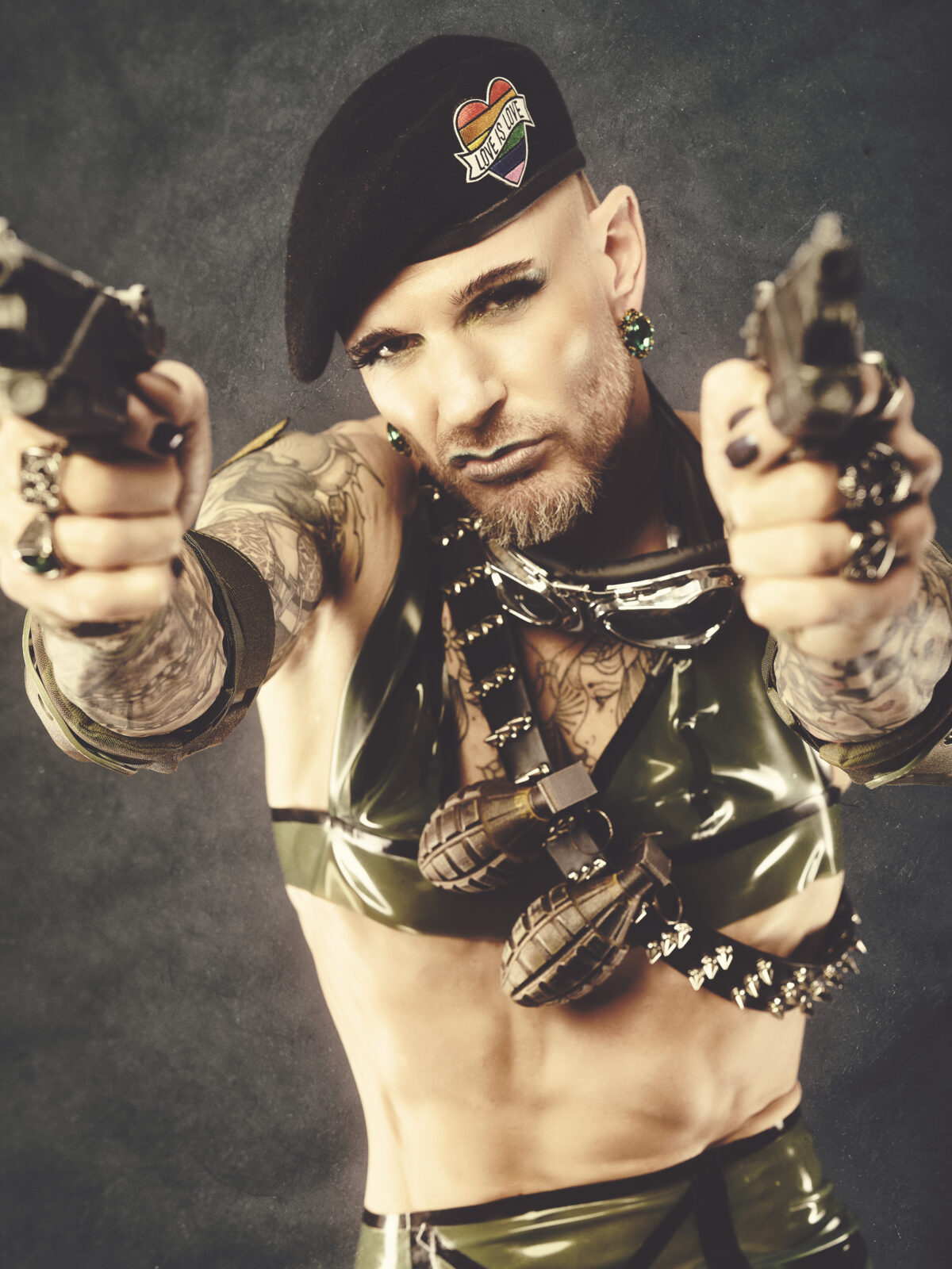 Queeres Fetischporträt mit Pistolen, Militärhut und Granatenschmuck – Studiofoto von Hell On Heels aus Düsseldorf und Köln